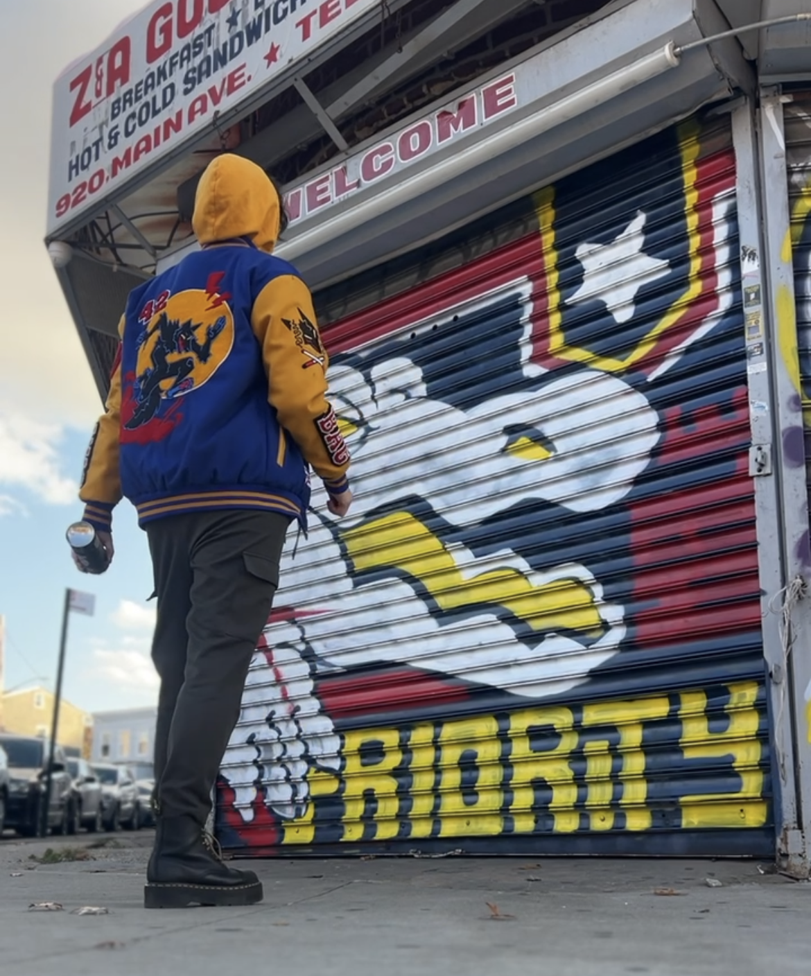Person wearing a colorful jacket standing in front of a mural on a storefront.